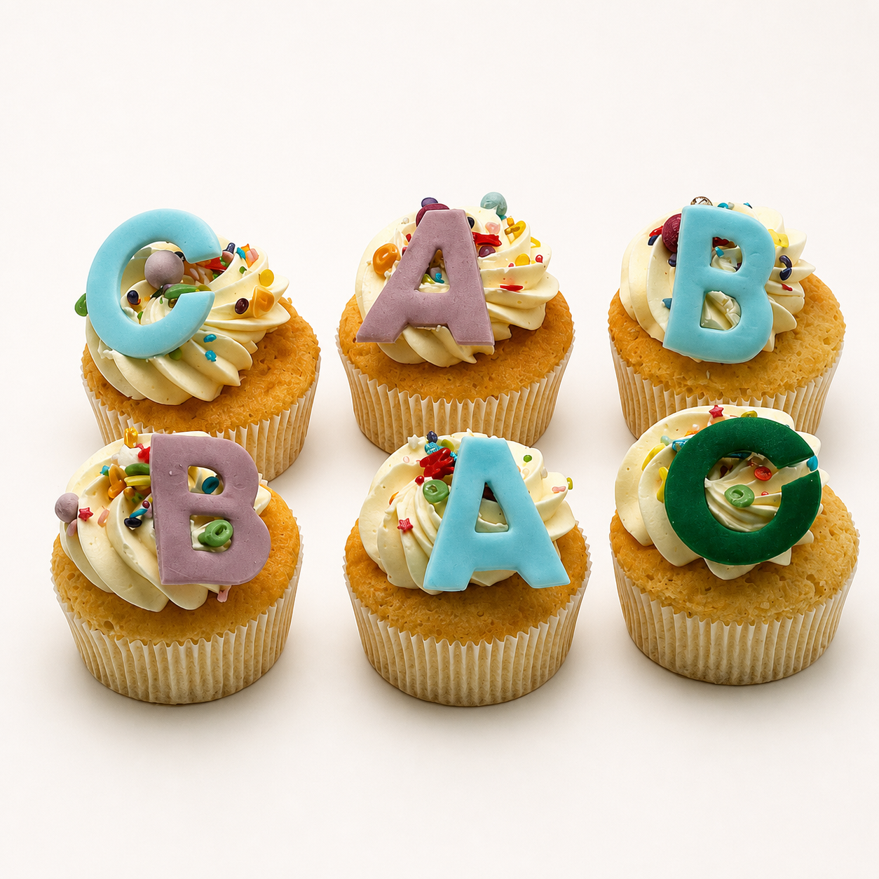 Einschulungs-Cupcakes – Produktfoto Sechs liebevoll dekorierte Einschulungs-Cupcakes mit ABC-Buchstaben vor fast weißem Hintergrund