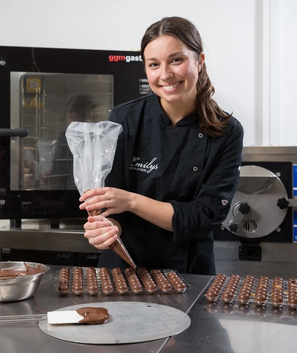 Konditorin Jana füllt in der Backstube Pralinenformen mit Schokolade